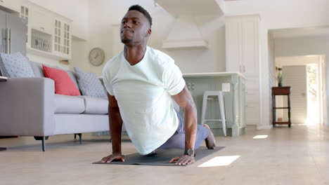 Hombre-Afroamericano-Enfocado-Haciendo-Flexiones-En-Una-Sala-De-Estar-Soleada,-Cámara-Lenta