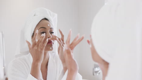 Mujer-Birracial-Aplicando-Crema-Facial-Mirando-En-El-Espejo-Del-Baño,-Cámara-Lenta