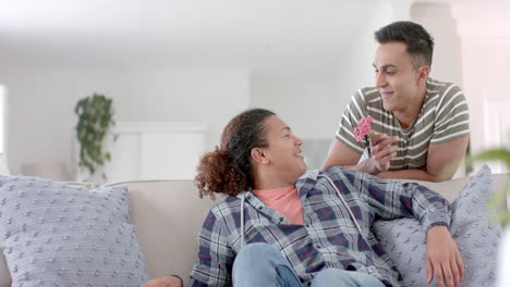 Happy-diverse-gay-male-couple-relaxing-on-couch-and-giving-flower,-copy-space,-slow-motion