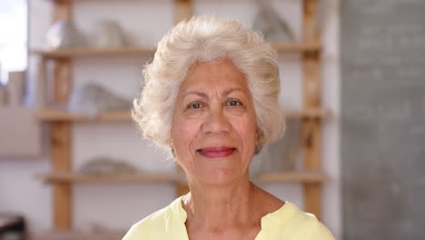 Feliz-Mujer-Birracial-Con-El-Pelo-Trenzado-Parada-Y-Sonriendo-En-Un-Estudio-De-Cerámica,-Cámara-Lenta