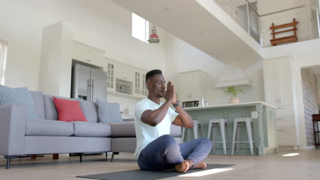 Hombre-Afroamericano-Enfocado-Practicando-Meditación-De-Yoga-En-Una-Sala-De-Estar-Soleada,-Cámara-Lenta