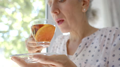 Thoughtful-senior-biracial-woman-drinking-tea-at-window-at-home,-slow-motion