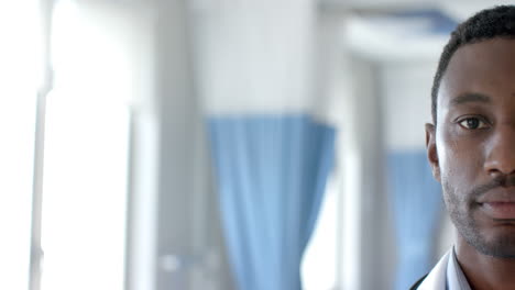 Half-portrait-of-african-american-male-doctor-smiling-in-hospital-ward,-copy-space,-slow-motion