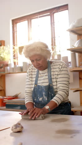 Happy-biracial-female-potter-with-gray-hair-shaping-clay-with-hands-in-pottery-studio,-slow-motion