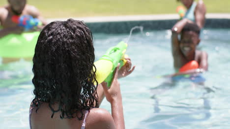 Feliz-Hermano-Y-Hermana-Afroamericanos-Jugando-Con-Pistolas-De-Agua-En-Una-Piscina-Soleada,-Cámara-Lenta