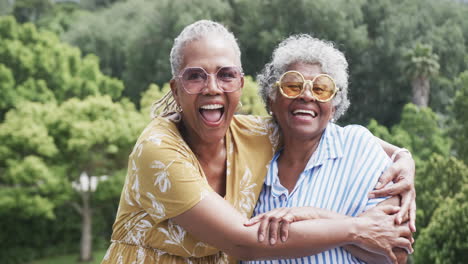 Retrato-De-Amigas-Afroamericanas-Mayores-Con-Gafas-De-Sol-Abrazándose-En-El-Jardín,-Cámara-Lenta