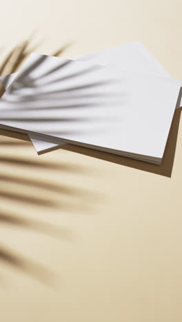 Vertical-video-of-shadow-of-plant-over-books-with-blank-pages-and-copy-space-on-yellow-background