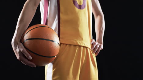 Female-basketball-player-in-a-basketball-uniform-holds-a-ball-on-a-black-background