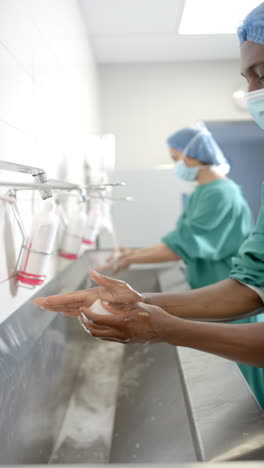 Vertical-video-of-diverse-female-and-male-surgeons-washing-hands-thoroughly,-slow-motion