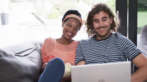 Diverse-couple,-a-young-African-American-woman-and-a-young-Caucasian-man,-watching-a-movie-on-a-lapt