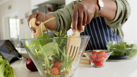 Mujer-Mayor-Afroamericana-Mezclando-Ensalada-En-Una-Cocina-Soleada,-Cámara-Lenta