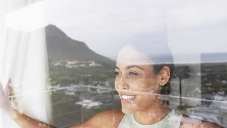 Happy-biracial-woman-looking-through-window-at-home,-slow-motion