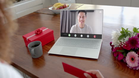 Caucasian-woman-holding-red-envelope-and-using-laptop-with-caucasian-man-on-screen