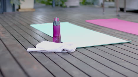 Water-bottle,-towel-and-exercise-mats-on-sunny-terrace