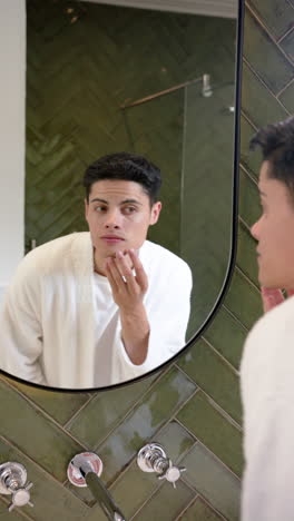 Vertical-video-of-biracial-man-inspecting-face-in-bathroom-mirror,-copy-space,-slow-motion