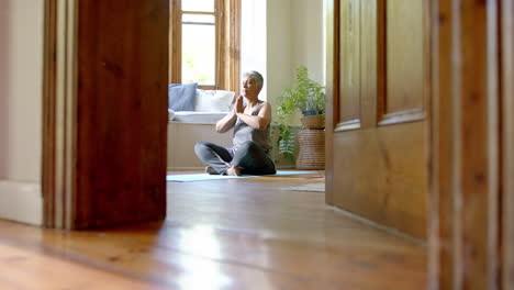 Focused-senior-biracial-woman-meditating-on-yoga-mat-at-home