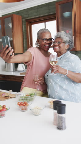 Vertical-video-of-happy-senior-african-american-female-friends-taking-selfie-in-kitchen,-slow-motion