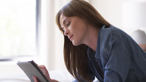 Middle-aged-Caucasian-woman-reads-on-a-tablet-at-home,-with-copy-space