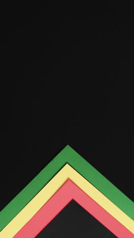 Vertical-video-of-red,-yellow-and-green-papers-with-copy-space-on-black-background