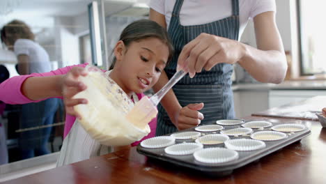 Glückliche-Biracial-Mutter-Und-Tochter-Gießen-Kuchenmischung-In-Kuchenformen-In-Der-Küche,-Zeitlupe