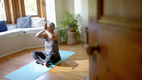 Focused-senior-biracial-woman-meditating-on-yoga-mat-at-home