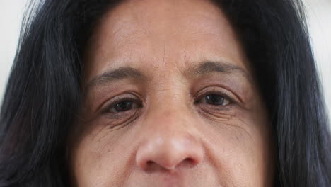 Eyes-of-happy-biracial-senior-woman-standing-and-smiling-in-sunny-room-at-home,-slow-motion