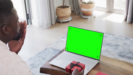 Hombre-Afroamericano-Sosteniendo-Un-Regalo-Rojo-Y-Usando-Una-Computadora-Portátil-Con-Espacio-Para-Copiar-En-Pantalla-Verde