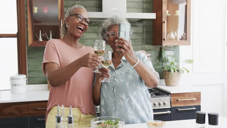 Felices-Amigas-Afroamericanas-Mayores-Bebiendo-Vino-Tomando-Selfies-En-La-Cocina,-Cámara-Lenta