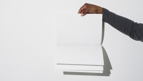 Video-of-hand-of-african-american-man-holding-book-with-blank-pages,-copy-space-on-white-background