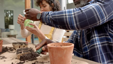 Happy-diverse-mature-couple-potting-and-watering-seedlings-on-garden-terrace,-slow-motion