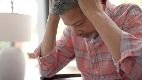 Worried-senior-biracial-man-sitting-with-head-in-hands-in-living-room,-slow-motion