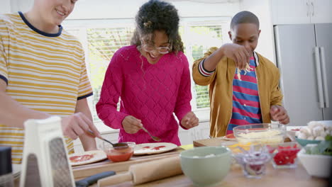 Happy-diverse-group-of-teenage-friends-cooking-and-making-pizza-in-kitchen,-slow-motion