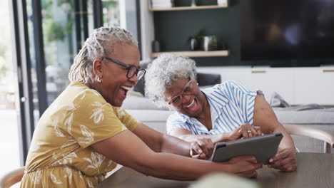 Felices-Amigas-Afroamericanas-Mayores-Usando-Tableta-Y-Riéndose-En-El-Comedor,-Cámara-Lenta