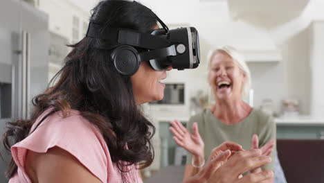 Fröhliche,-Vielfältige-Seniorinnen-Mit-VR-Brille-Und-Lachen-Im-Sonnigen-Wohnzimmer,-Zeitlupe