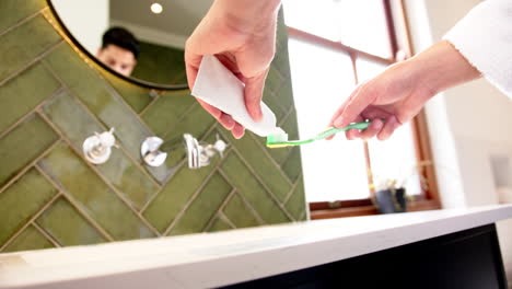 Midsection-of-biracial-man-putting-toothpaste-on-toothbrush-in-bathroom,-slow-motion