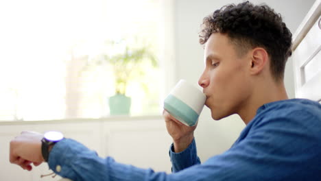 Hombre-Birracial-Tomando-Café-Sentado-En-El-Suelo-En-La-Cocina-De-Casa,-En-Cámara-Lenta