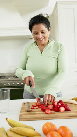 Feliz-Mujer-Mayor-Birracial-Cortando-Frutas-Y-Sonriendo-En-Una-Cocina-Soleada,-Cámara-Lenta