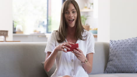 Middle-aged-Caucasian-woman-sits-on-a-sofa-at-home,-blowing-a-kiss-on-video-call