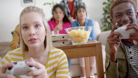 Happy-diverse-group-of-teenage-friends-sitting-on-couch-and-playing-video-games-at-home,-slow-motion