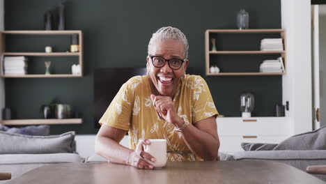 Glückliche-ältere-Afroamerikanische-Frau-In-Einer-Brille,-Die-Zu-Hause-Einen-Videoanruf-Mit-Kaffee-Und-Zeitlupe-Führt