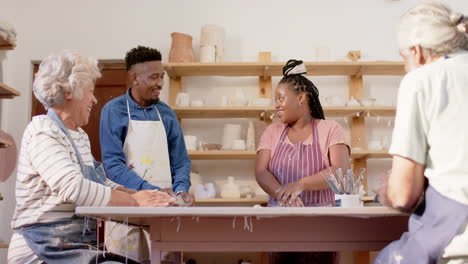 Happy-diverse-group-of-potters-shaping-clay-with-hands-and-discussing-in-pottery-studio