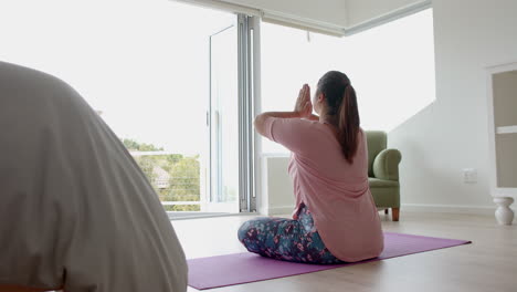 Plus-size-biracial-woman-sitting-on-floor-practicing-yoga-meditation,-copy-space,-slow-motion