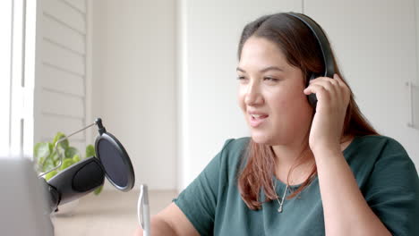 Happy-plus-size-biracial-woman-in-headphones-podcasting-with-laptop-at-home,-copy-space,-slow-motion