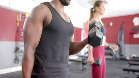 Colocar-A-Un-Hombre-Afroamericano-Y-A-Una-Joven-Caucásica-Haciendo-Ejercicio-En-El-Gimnasio,-Levantando-Pesas