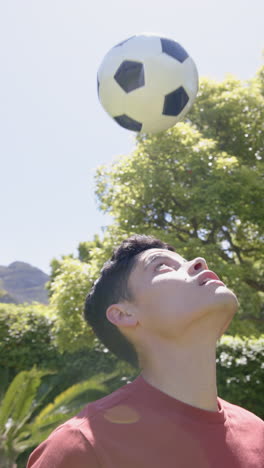 Vertical-video-of-biracial-man-practicing-football-skills-in-sunny-garden,-copy-space,-slow-motion