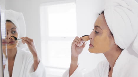 Mujer-Birracial-Feliz-Aplicando-Mascarilla-De-Belleza-Mirando-En-El-Espejo-En-El-Baño,-Cámara-Lenta