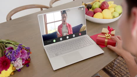 Caucasian-woman-holding-gift-and-talking-with-caucaslan-woman-on-laptop-screen