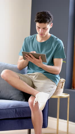 Vertical-video-of-biracial-man-sitting-in-living-room-using-tablet,-slow-motion