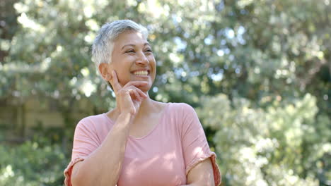 Retrato-De-Una-Feliz-Mujer-Birracial-Mayor-Con-El-Pelo-Corto-En-Un-Jardín-Soleado-En-Casa,-Cámara-Lenta