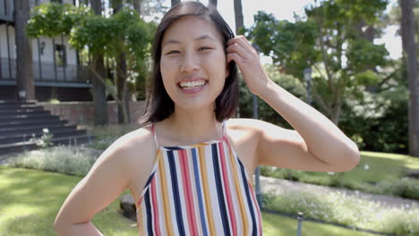 Glückliche-Asiatische-Frau-Mit-Dunklem-Glattem-Haar,-Die-Im-Sonnigen-Garten-Steht-Und-Lächelt,-Zeitlupe